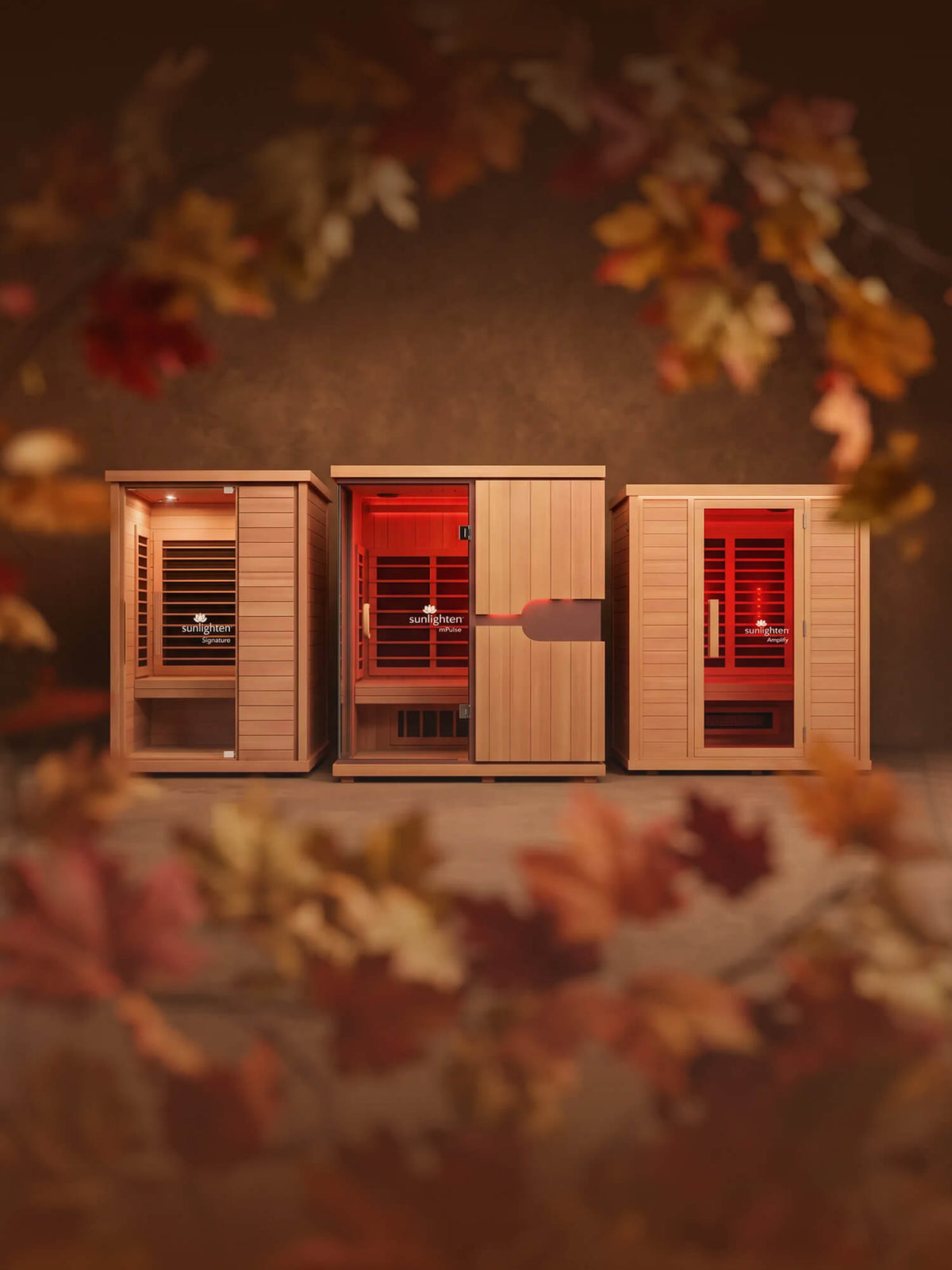Three Sunlighten cabin saunas shown against a autumn backdrop surrounded by leaves.